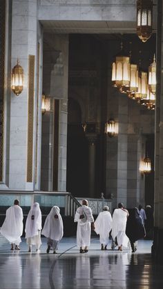 several men in white robes are walking through a building with chandeliers hanging from the ceiling