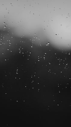 black and white photo of raindrops on window with dark sky in the background