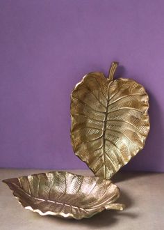 a golden leaf shaped bowl sitting on top of a table next to a purple wall