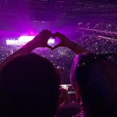 two people making a heart with their hands in front of an audience at a concert