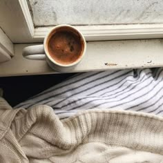 a cup of coffee sitting on top of a window sill next to a blanket