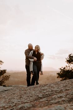 a man and woman standing on top of a hill next to each other with trees in the background