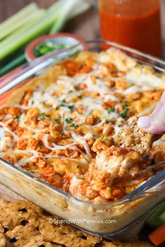 a hand dipping some food into a casserole dish with crackers on the side