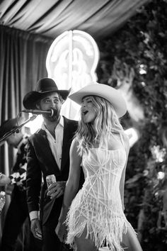 a man standing next to a woman in a white dress and cowboy hat at a party