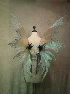 a white mannequin with blue and green fairy wings on it's head