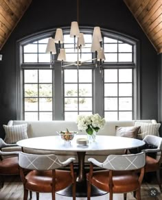 a dining room table with four chairs around it and a couch in front of the window