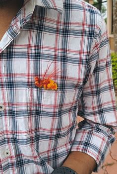 a close up of a person wearing a plaid shirt with an orange flower in the pocket