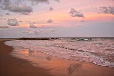 an ocean beach with waves coming in to the shore and clouds above it at sunset