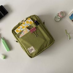 an open green bag sitting on top of a white table next to other items and office supplies