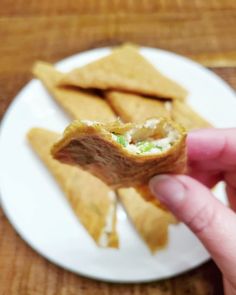 a hand holding up a piece of food on a white plate next to some pita chips