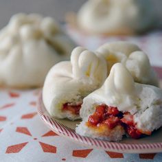 some dumplings are on a plate and one is covered in white icing, the other has red sauce