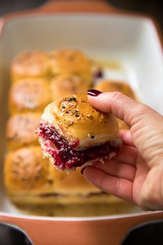 a hand holding a small sandwich in front of some other muffins on a plate