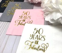 napkins with gold lettering on them and white flowers in the background, some are folded to say 50 years of fabulous