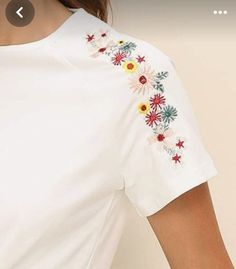 a woman wearing a white t - shirt with colorful flowers on the sleeves and shoulder