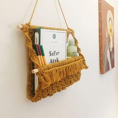 a book shelf hanging on the wall with books and pens in it, next to a painting