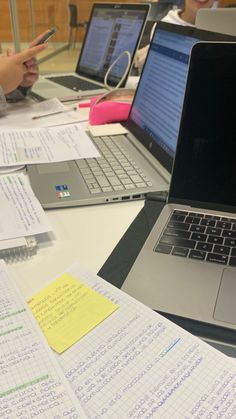 two laptops are sitting on a table with papers and pens in front of them