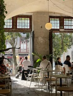 people are sitting at tables in an open area with large windows and potted plants