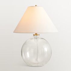 a clear glass lamp with a white shade on it's base and a light bulb