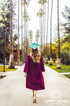 a woman wearing a graduation cap and gown walks down a path in front of palm trees