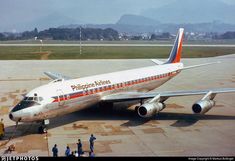 an airplane is parked on the tarmac with people standing around it and mountains in the background