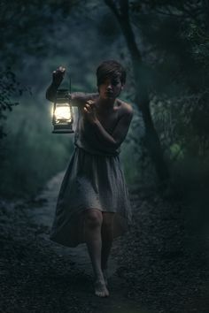 a woman holding a lantern walking down a path in the woods at night with light shining on her face