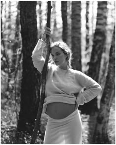 a woman standing in the woods holding onto a tree branch