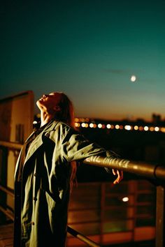 a woman standing on top of a roof looking up at the sky with her eyes closed