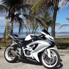 a white and black motorcycle parked in front of palm trees on the beach near the ocean