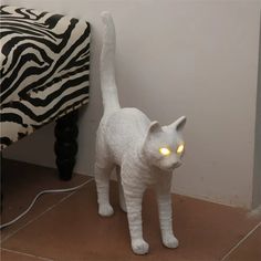 a white cat with glowing eyes standing in front of a zebra print bed spread on the floor