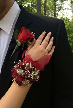 a close up of a person wearing a suit and holding a red rose wrist corsage