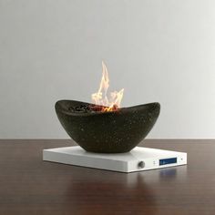 a fire bowl sitting on top of a wooden table next to a white clock and remote control