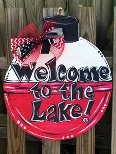 a welcome to the lake sign hanging from a wooden fence with a bow on it