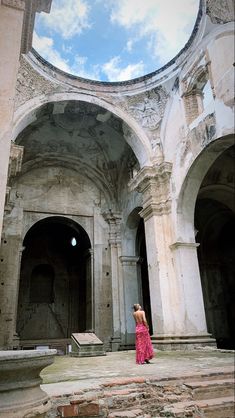 a woman in a red dress is standing inside an old building and looking up at the sky