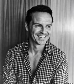 a black and white photo of a man with a smile on his face, wearing a checkered shirt