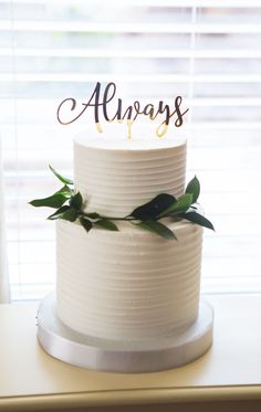 a white cake with the word alwayss on it sitting on a table in front of a window