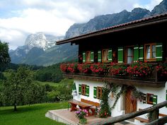 a house with green shutters and red flowers on the balconies