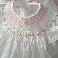 a white dress with pink roses on the neckline and collar, sitting on a table