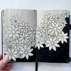 a hand holding an open notebook with flowers drawn on the pages and in front of it