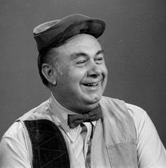 an old photo of a man with a hat on his head and suspenders smiling