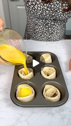 a person pouring orange juice into a muffin tin filled with rolled up pastries