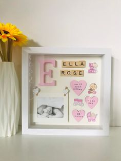 a baby's name frame with flowers and a vase on the table next to it