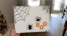 a hand holding up a halloween card with spider webs on it and boo written in orange