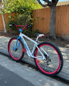 a white bicycle with red and blue rims parked on the sidewalk