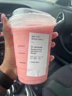 a person holding up a pink drink in their hand with information on the cup sleeve