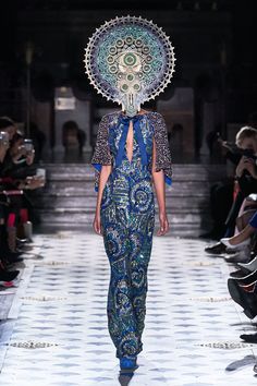 a model walks down the runway in a blue dress with an umbrella on her head