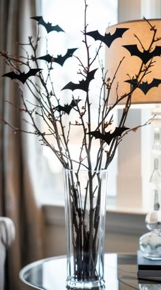 a glass vase filled with branches and bats on top of a table next to a lamp