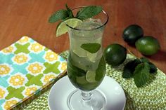 a glass filled with limeade and mint on top of a white plate next to green leaves