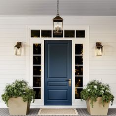 two planters with flowers in front of a blue door on a white house porch