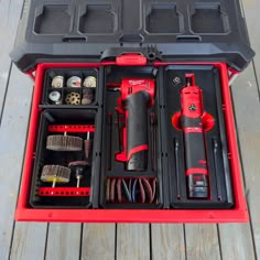 a red tool box filled with tools on top of a wooden floor next to a black case