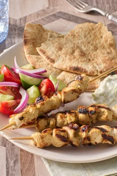 a white plate topped with chicken and veggies next to pita bread on top of a wooden table